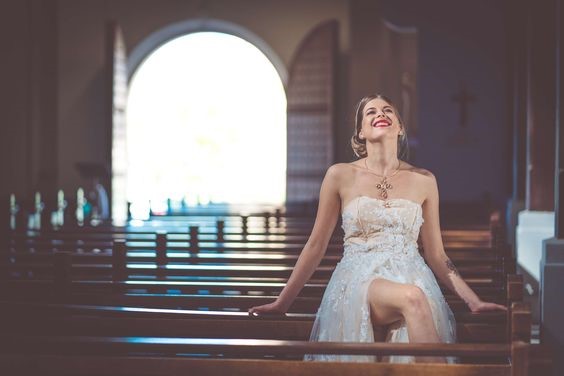 Photo d'une mariée, souriante, assise dans une église.
